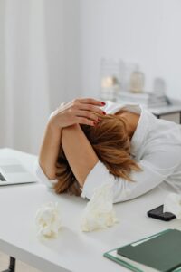 woman with an overwhelming mental load, putting her head on her desk with crumpled paper
